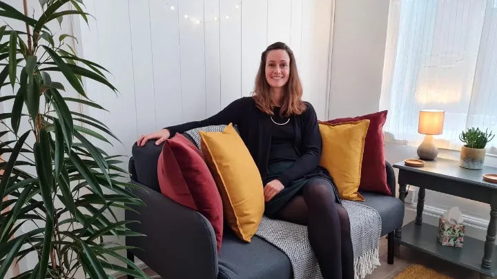 Photo of Kara Danks in her Newcastle Upon Tyne therapy room. She is sitting on a comfortable sofa surounded by cushions.