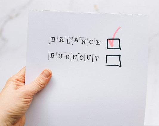 Hand holding a piece of paper with a checklist stating 'balance' and 'burnout' with the balance box ticked.
