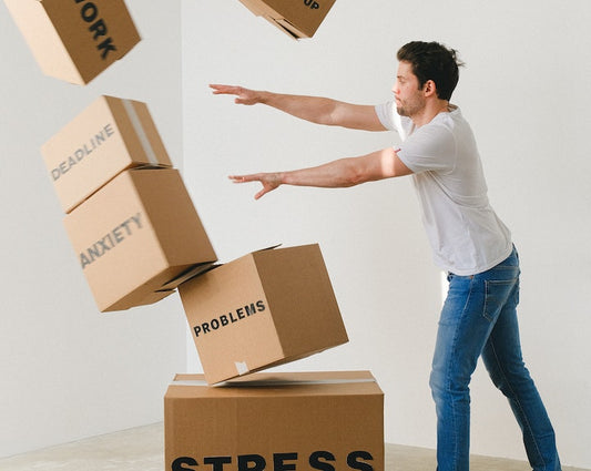 Man pushing over a pile of cardboard boxes labelled with 'stress', 'problems', 'anxiety', 'deadline', 'work' and 'break up'.