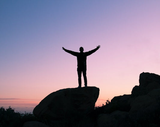 Person with arms outstretched stood on a mountain rock in awe at sunrise